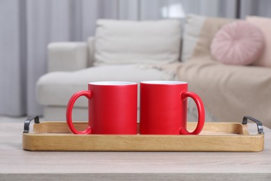 Photo of Blank red ceramic mugs on white wooden table. Mockup for design