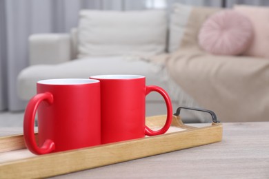 Photo of Blank red ceramic mugs on white wooden table. Mockup for design