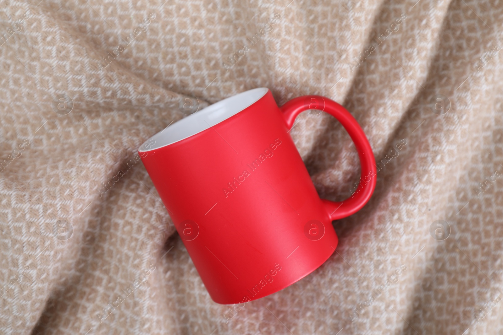 Photo of Blank red ceramic mug on beige fabric, top view. Mockup for design