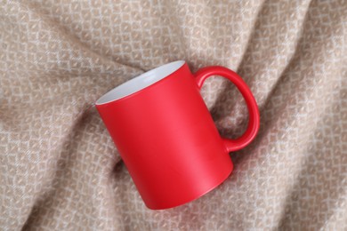 Photo of Blank red ceramic mug on beige fabric, top view. Mockup for design