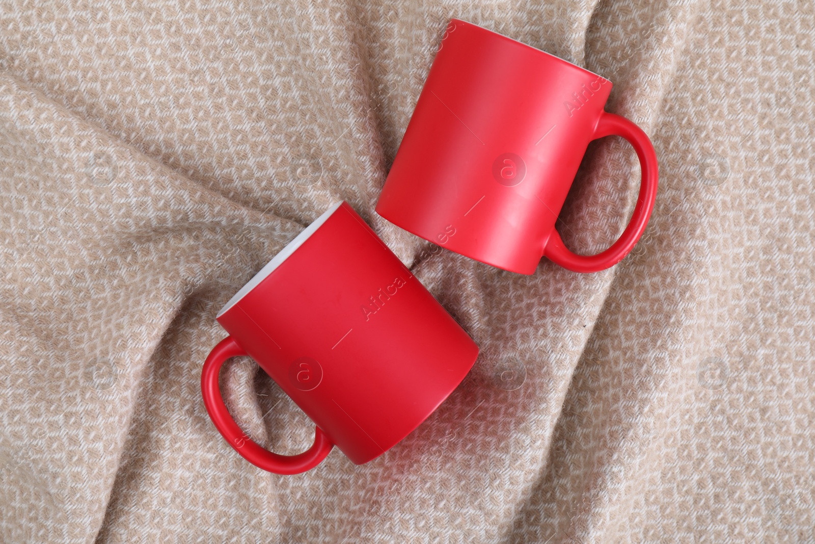 Photo of Blank red ceramic mugs on beige fabric, top view. Mockup for design