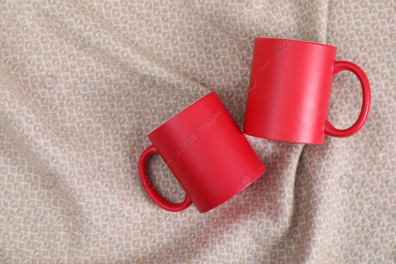 Photo of Blank red ceramic mugs on beige fabric, top view. Mockup for design