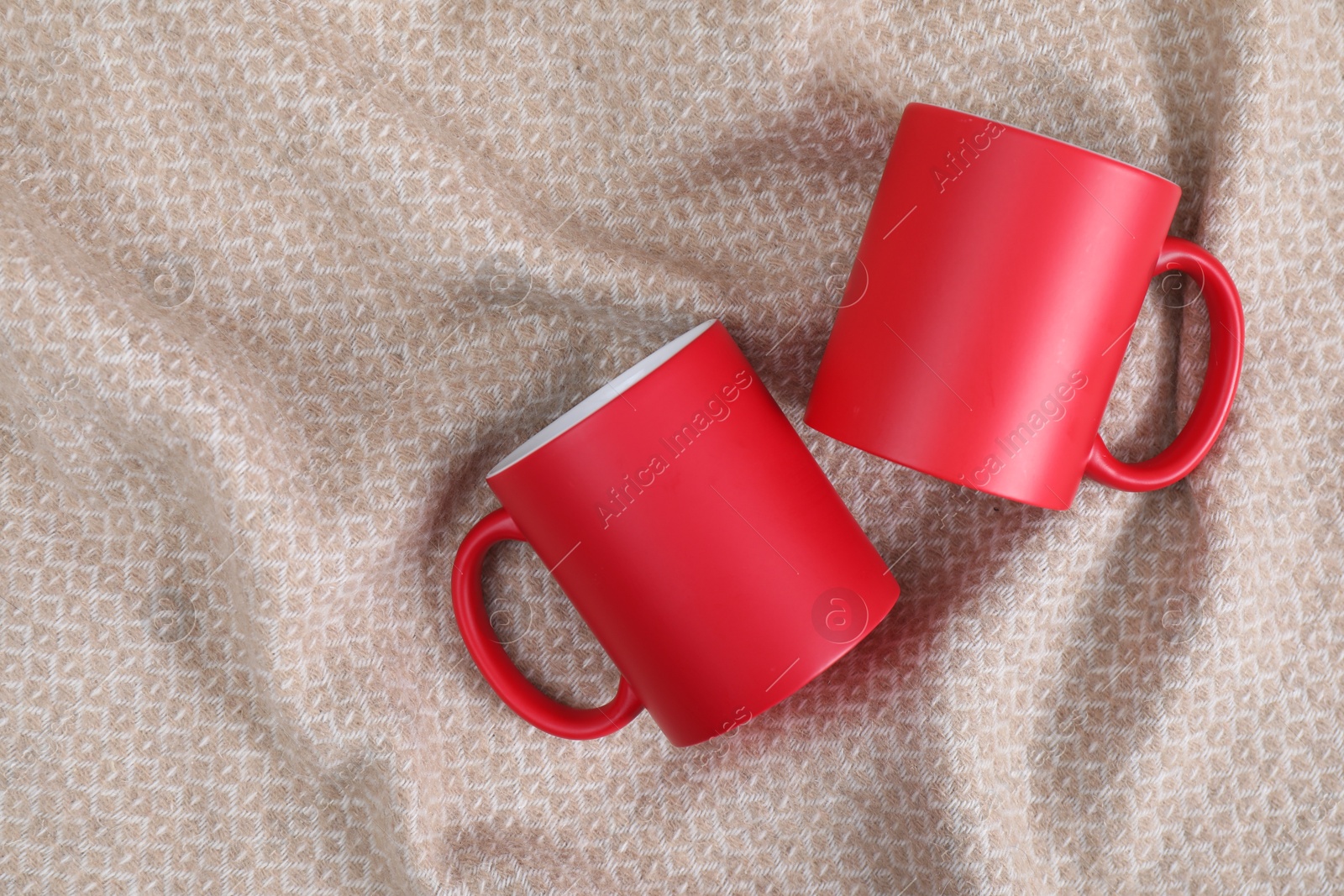 Photo of Blank red ceramic mugs on beige fabric, top view. Mockup for design