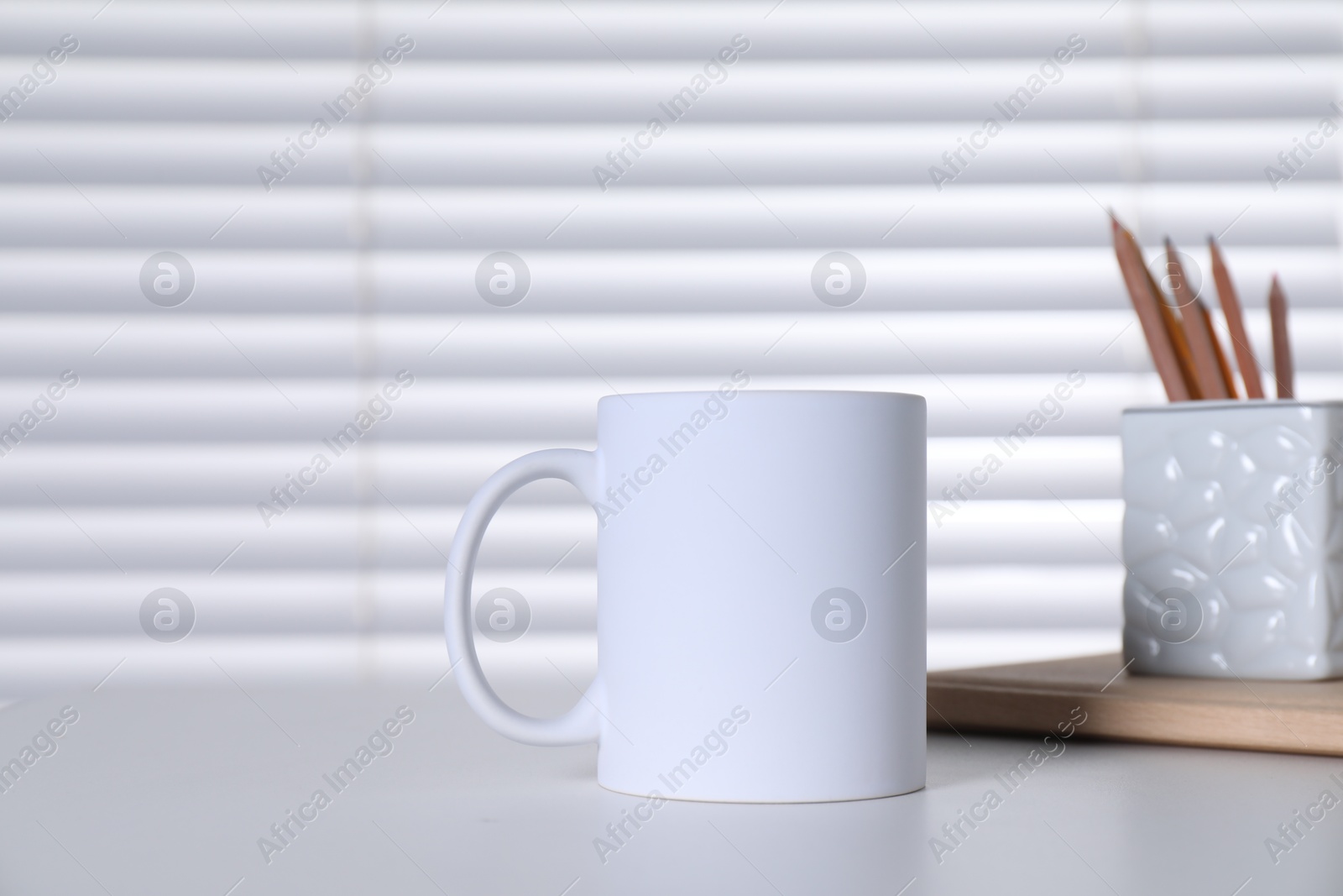 Photo of One blank ceramic mug and stationery on white table. Mockup for design