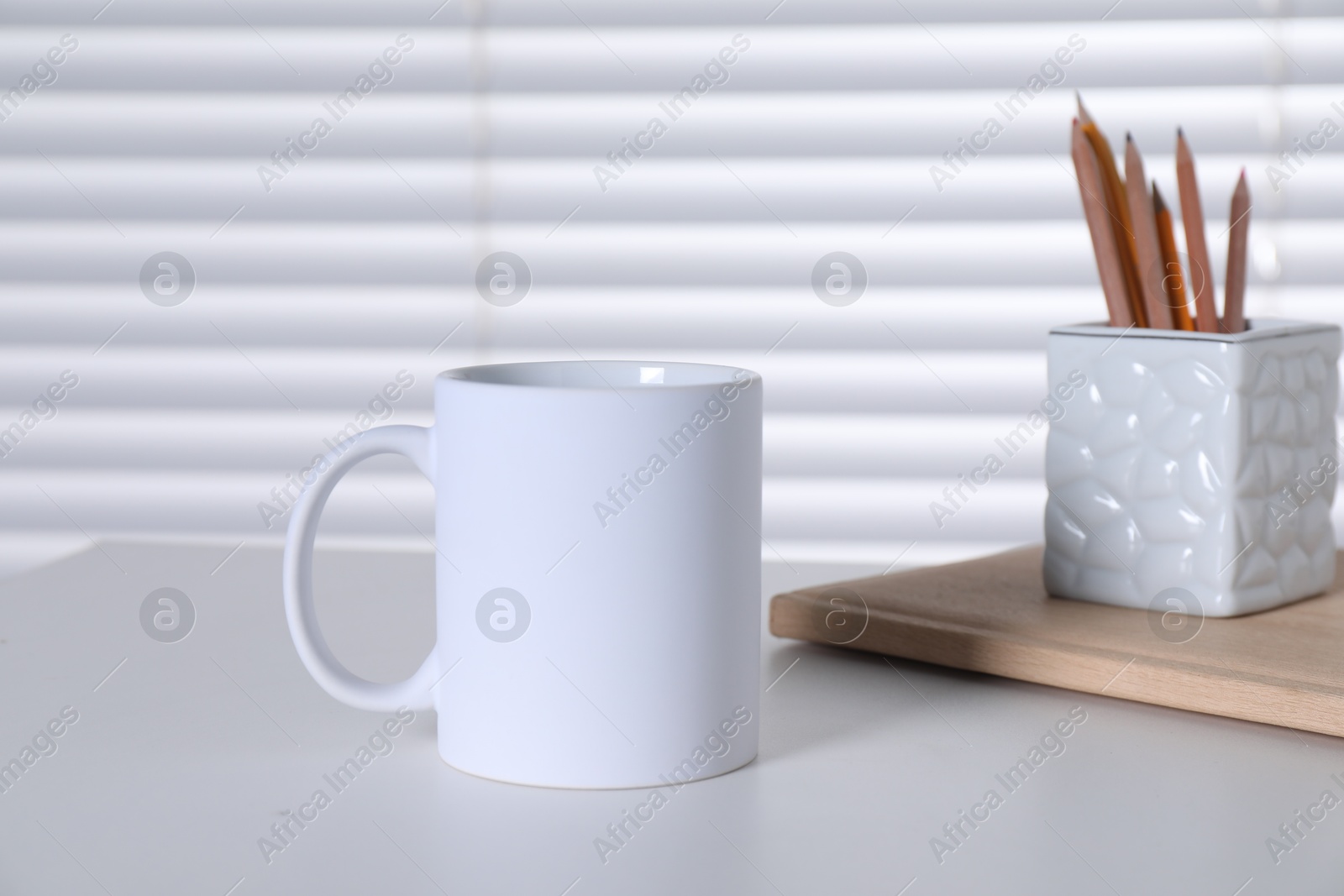 Photo of One blank ceramic mug and stationery on white table. Mockup for design