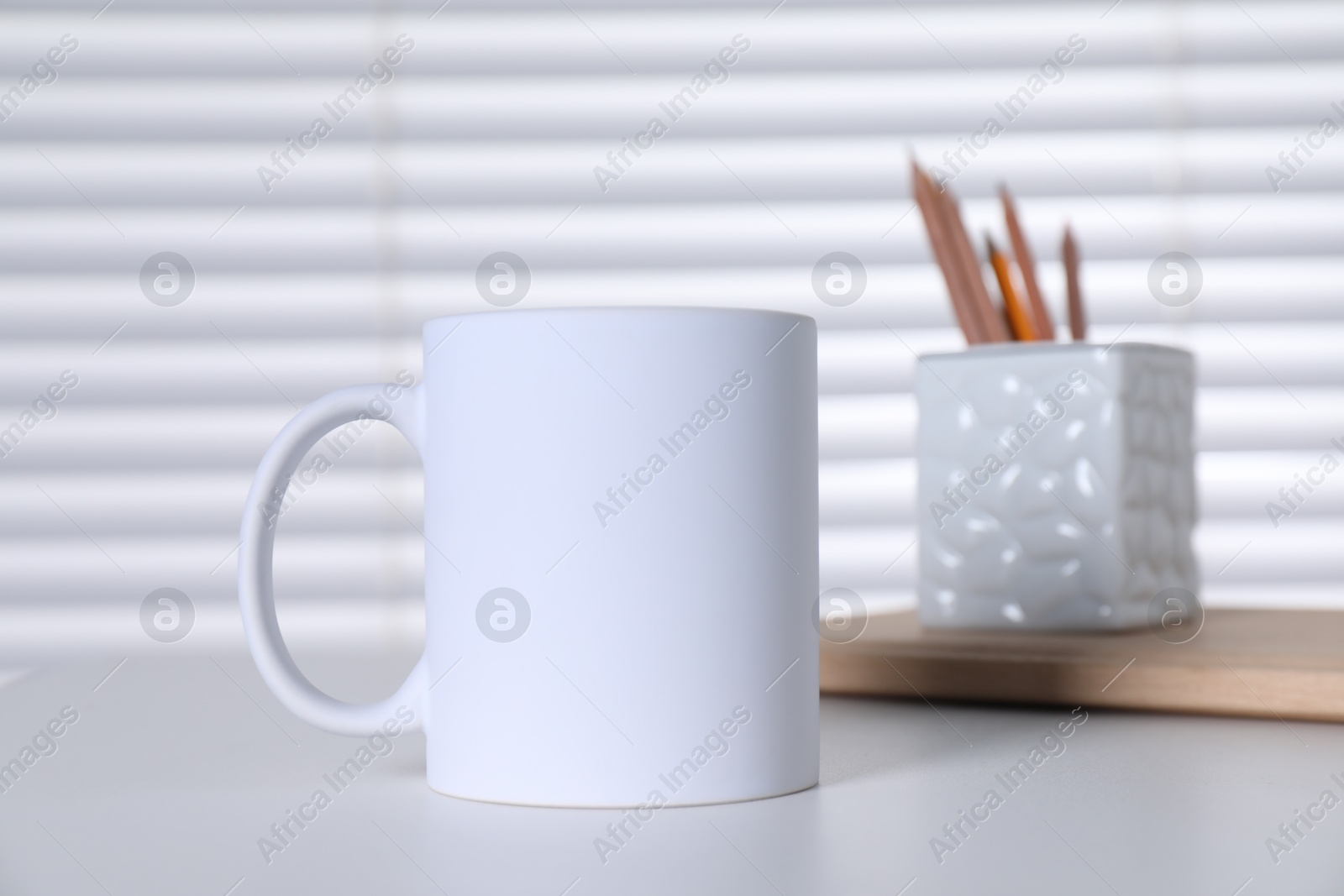 Photo of One blank ceramic mug and stationery on white table. Mockup for design