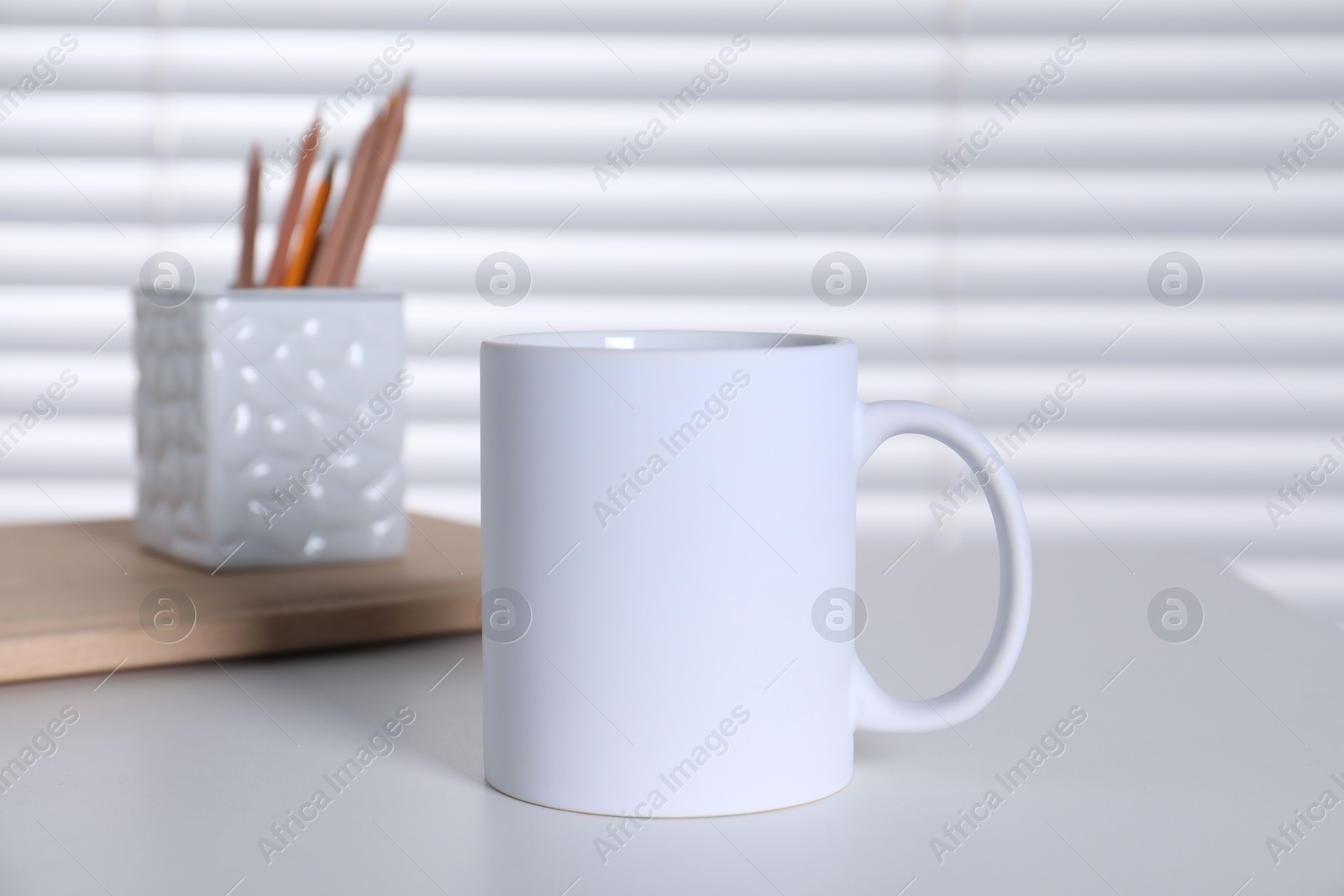 Photo of One blank ceramic mug and stationery on white table. Mockup for design