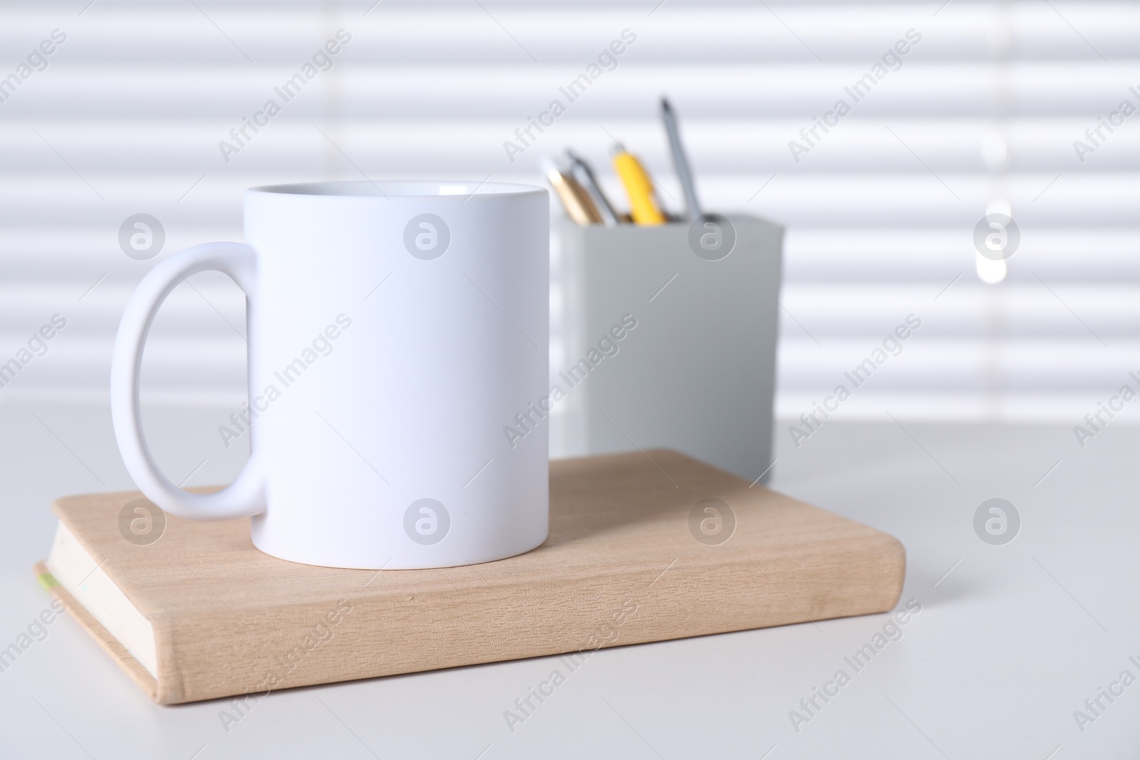 Photo of One blank ceramic mug and stationery on white table. Mockup for design