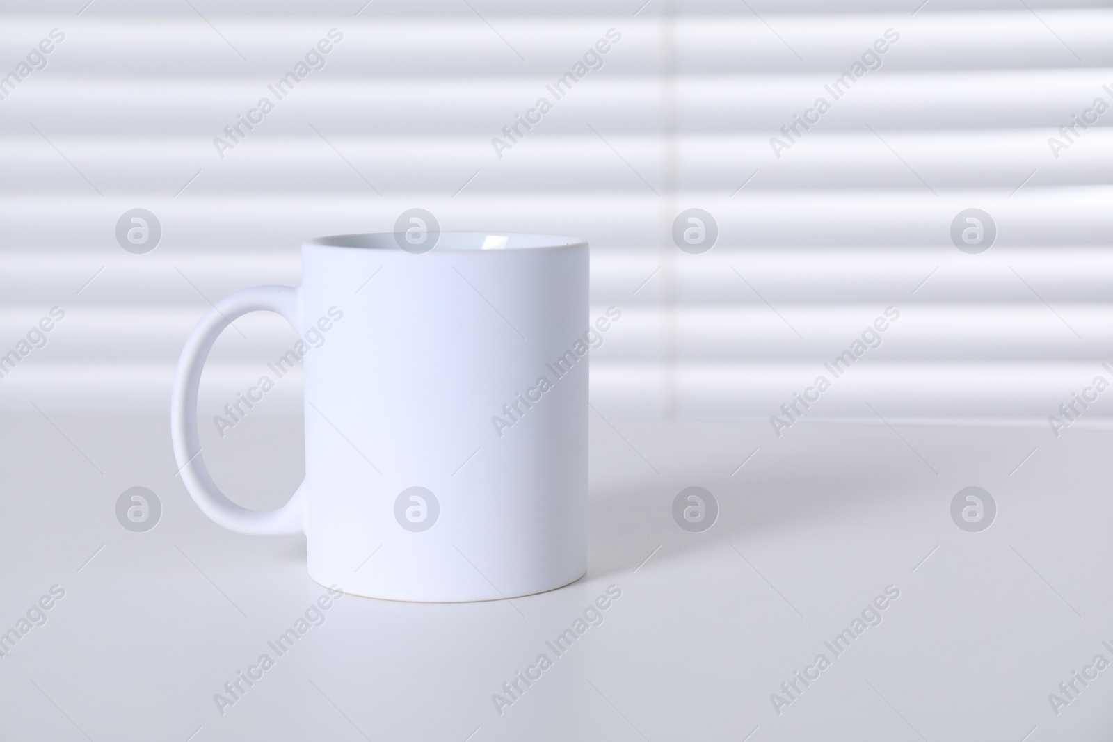 Photo of One blank ceramic mug on white table. Mockup for design