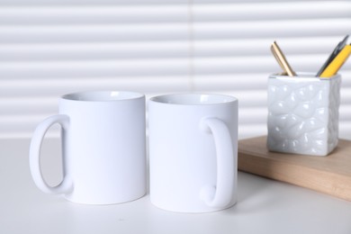 Photo of Blank ceramic mugs and stationery on white table. Mockup for design