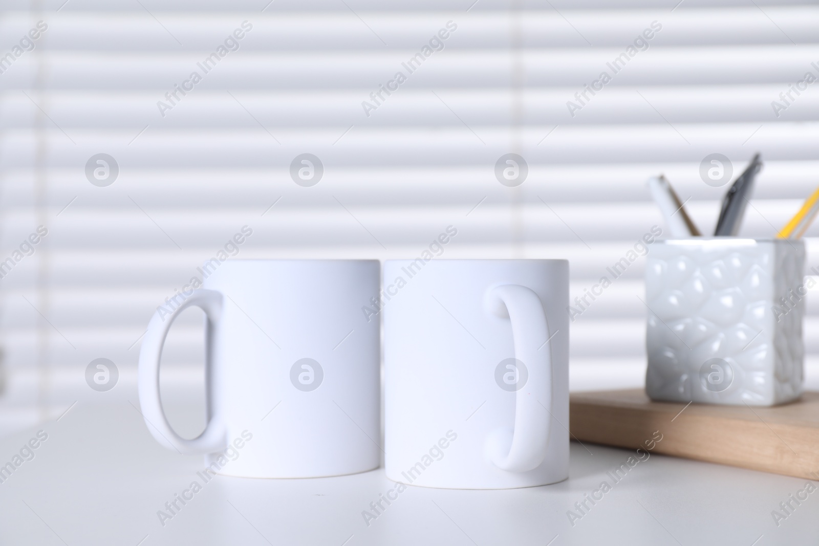 Photo of Blank ceramic mugs and stationery on white table. Mockup for design