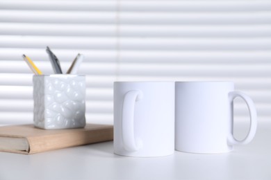 Blank ceramic mugs and stationery on white table. Mockup for design