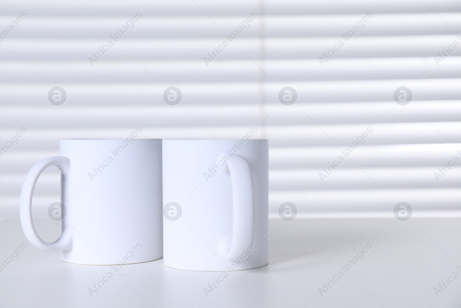 Photo of Blank ceramic mugs on white table. Mockup for design