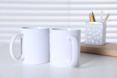 Blank ceramic mugs and stationery on white table. Mockup for design