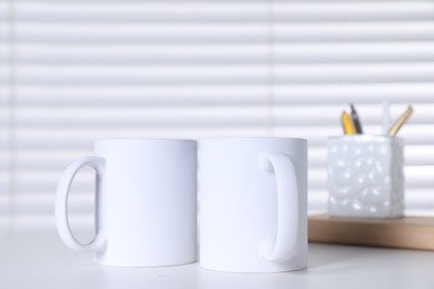 Photo of Blank ceramic mugs and stationery on white table. Mockup for design