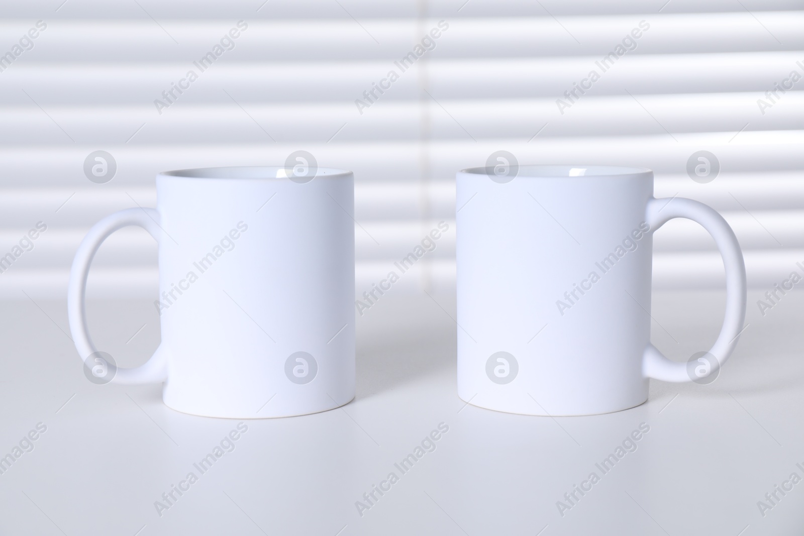 Photo of Blank ceramic mugs on white table. Mockup for design