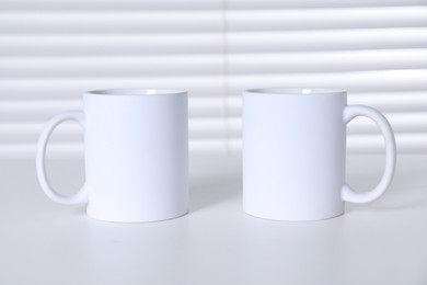 Blank ceramic mugs on white table. Mockup for design