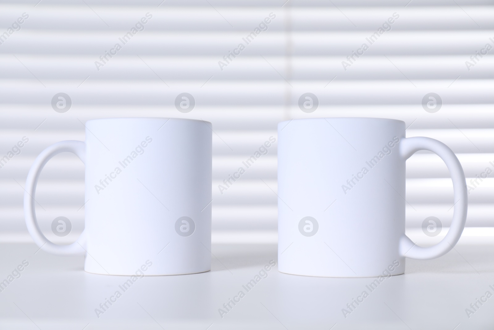 Photo of Blank ceramic mugs on white table. Mockup for design