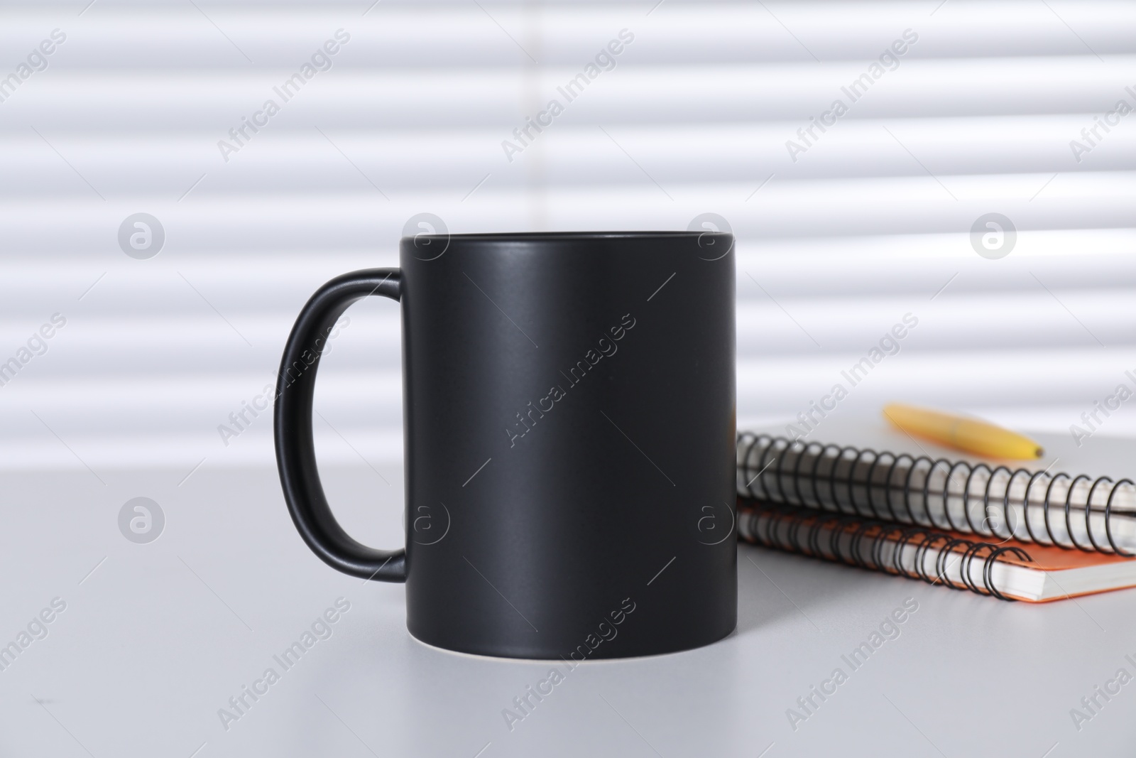 Photo of One blank black ceramic mug and stationery on white table. Mockup for design