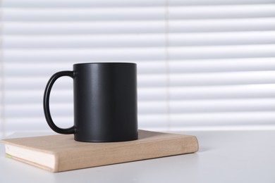 Photo of One blank black ceramic mug and notebook on white table. Mockup for design