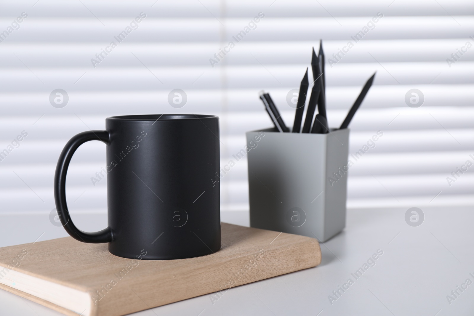 Photo of One blank black ceramic mug and stationery on white table. Mockup for design