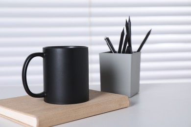 Photo of One blank black ceramic mug and stationery on white table. Mockup for design