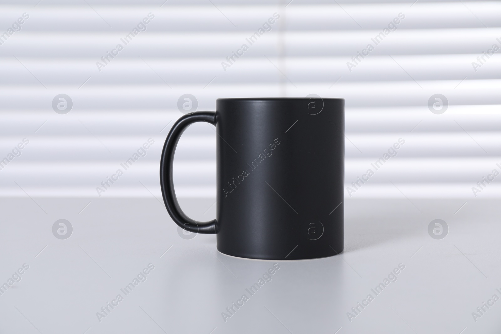 Photo of One blank black ceramic mug on white table. Mockup for design