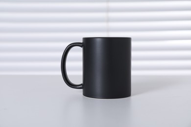 Photo of One blank black ceramic mug on white table. Mockup for design