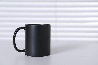 Photo of One blank black ceramic mug on white table. Mockup for design