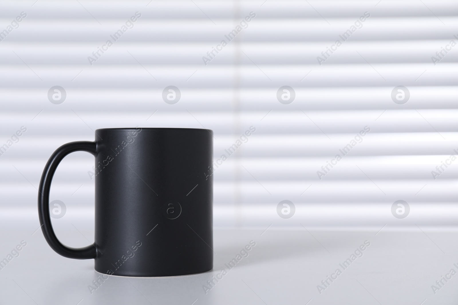 Photo of One blank black ceramic mug on white table. Mockup for design