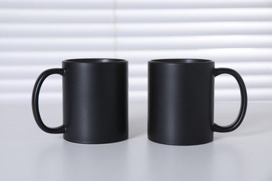 Photo of Blank black ceramic mugs on white table. Mockup for design