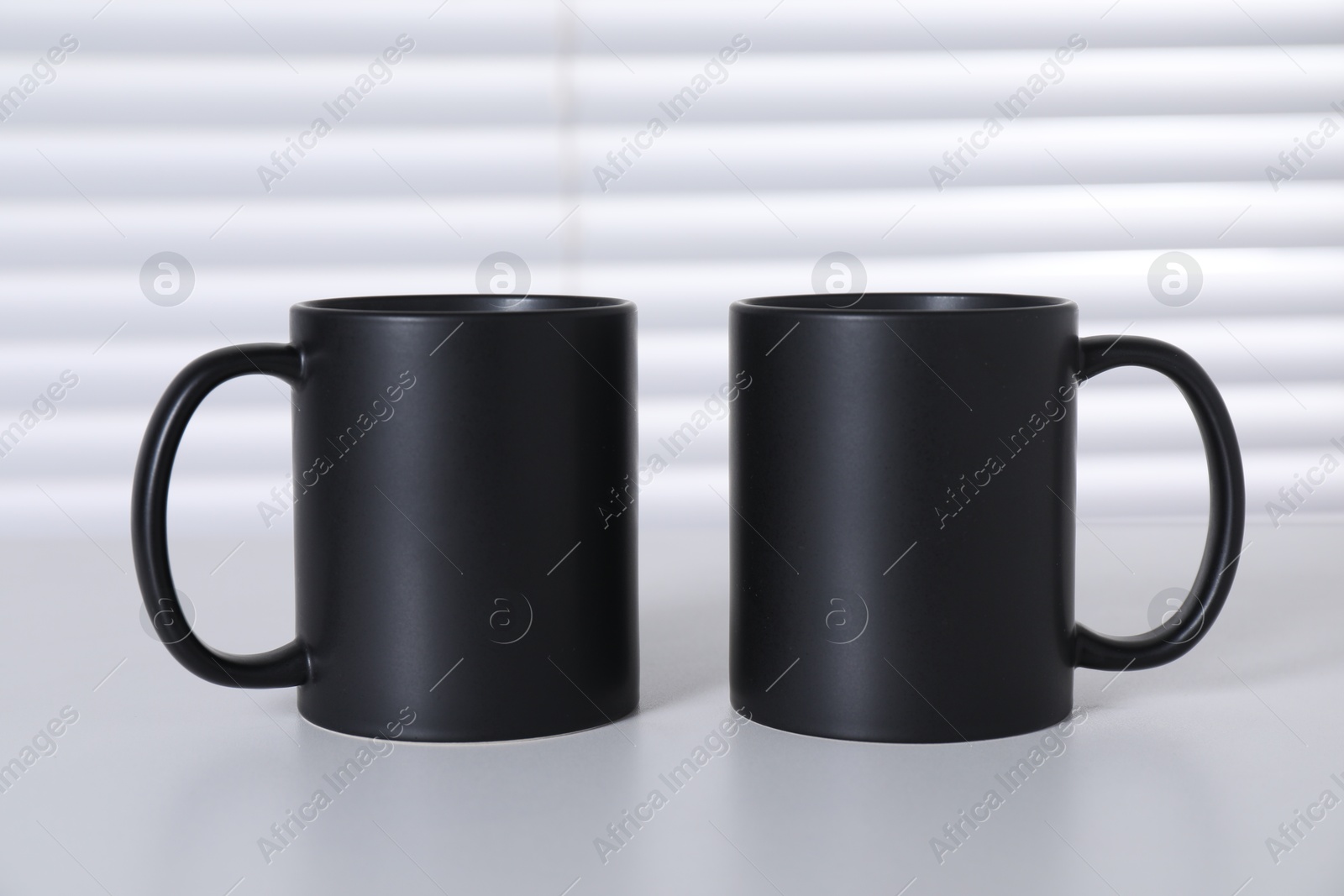 Photo of Blank black ceramic mugs on white table. Mockup for design