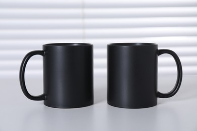 Photo of Blank black ceramic mugs on white table. Mockup for design