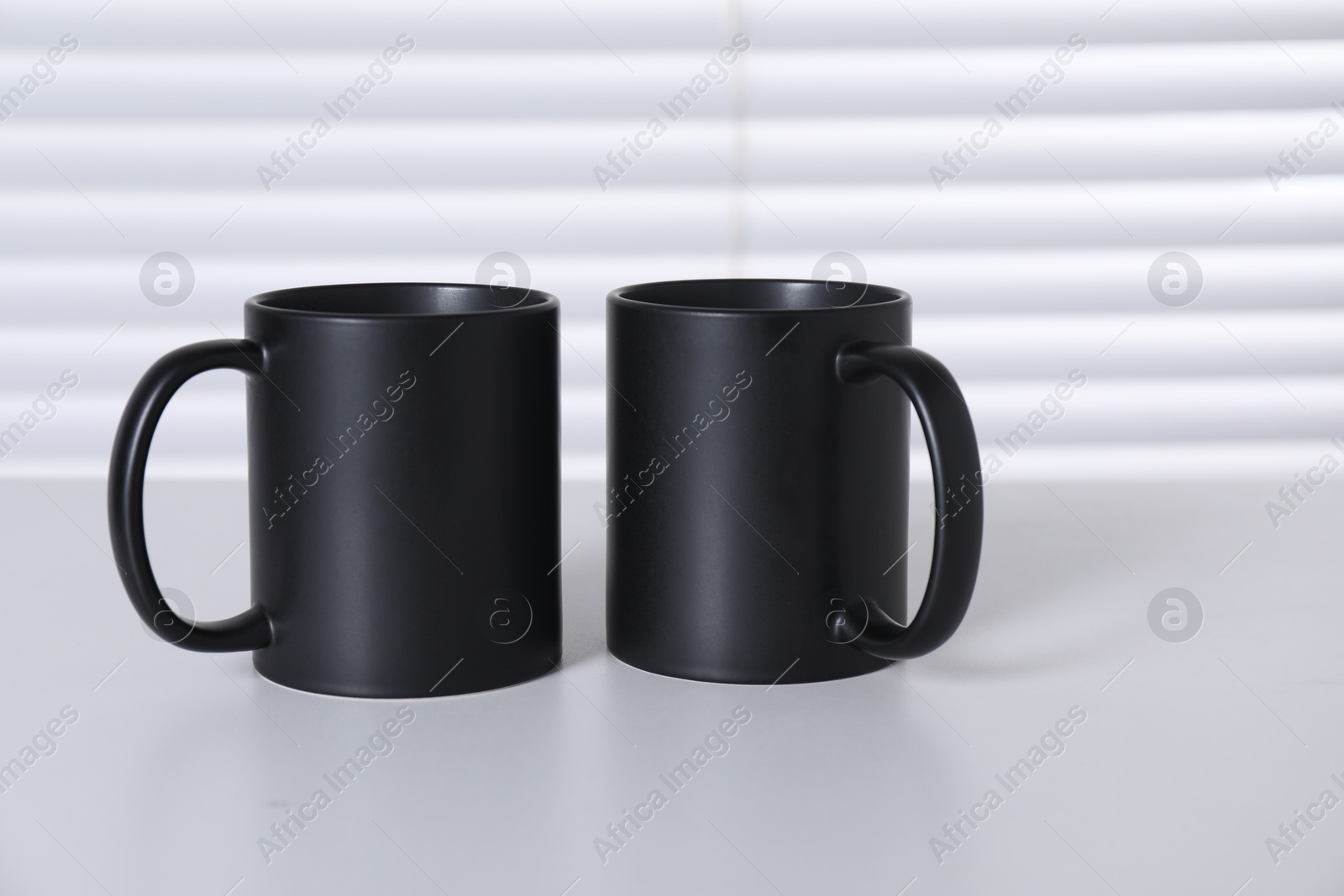 Photo of Blank black ceramic mugs on white table. Mockup for design