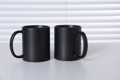 Blank black ceramic mugs on white table. Mockup for design