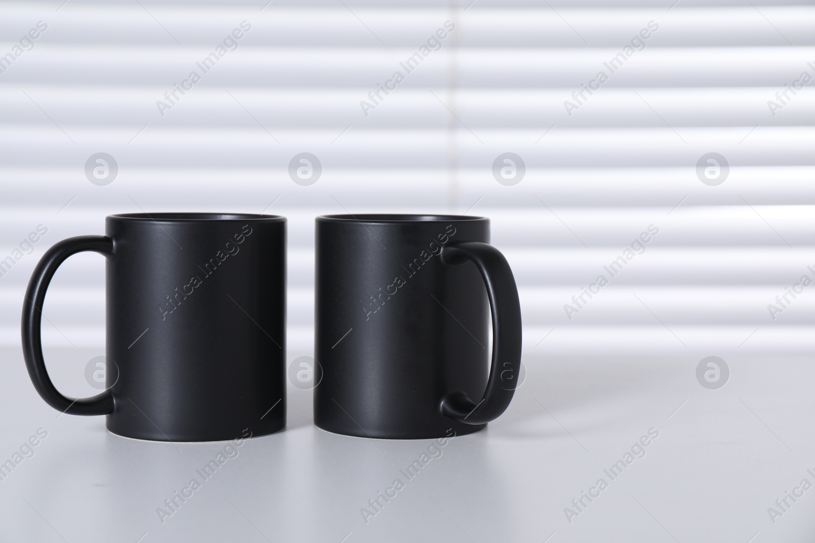 Photo of Blank black ceramic mugs on white table. Mockup for design