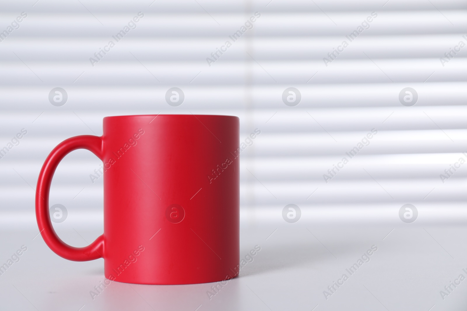 Photo of One blank red ceramic mug on white table. Mockup for design