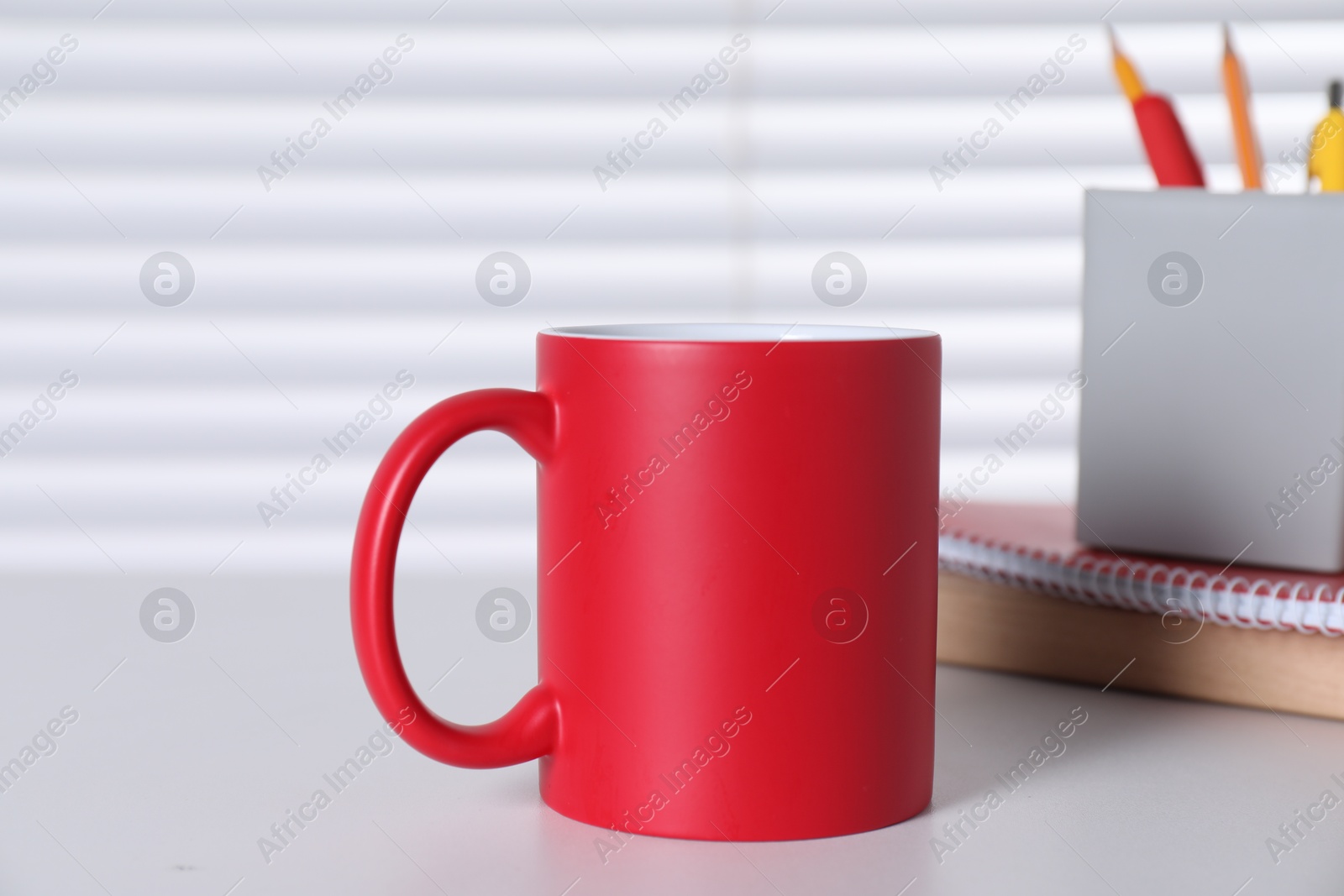 Photo of One blank red ceramic mug on white table. Mockup for design