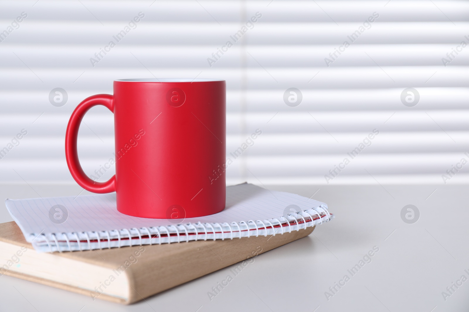 Photo of One blank red ceramic mug and notebooks on white table. Mockup for design