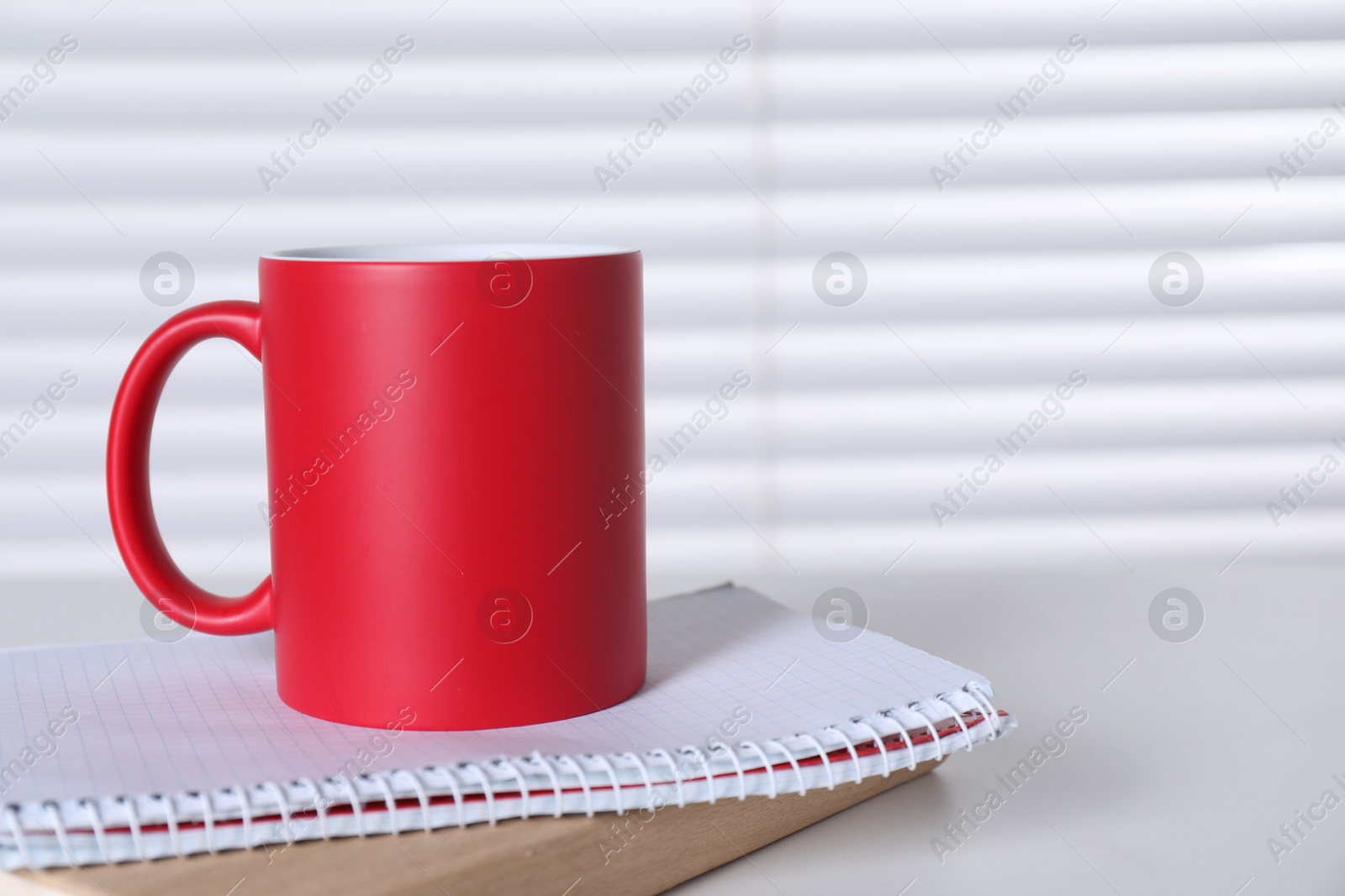 Photo of One blank red ceramic mug and notebooks on white table. Mockup for design