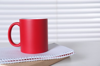 Photo of One blank red ceramic mug and notebooks on white table. Mockup for design