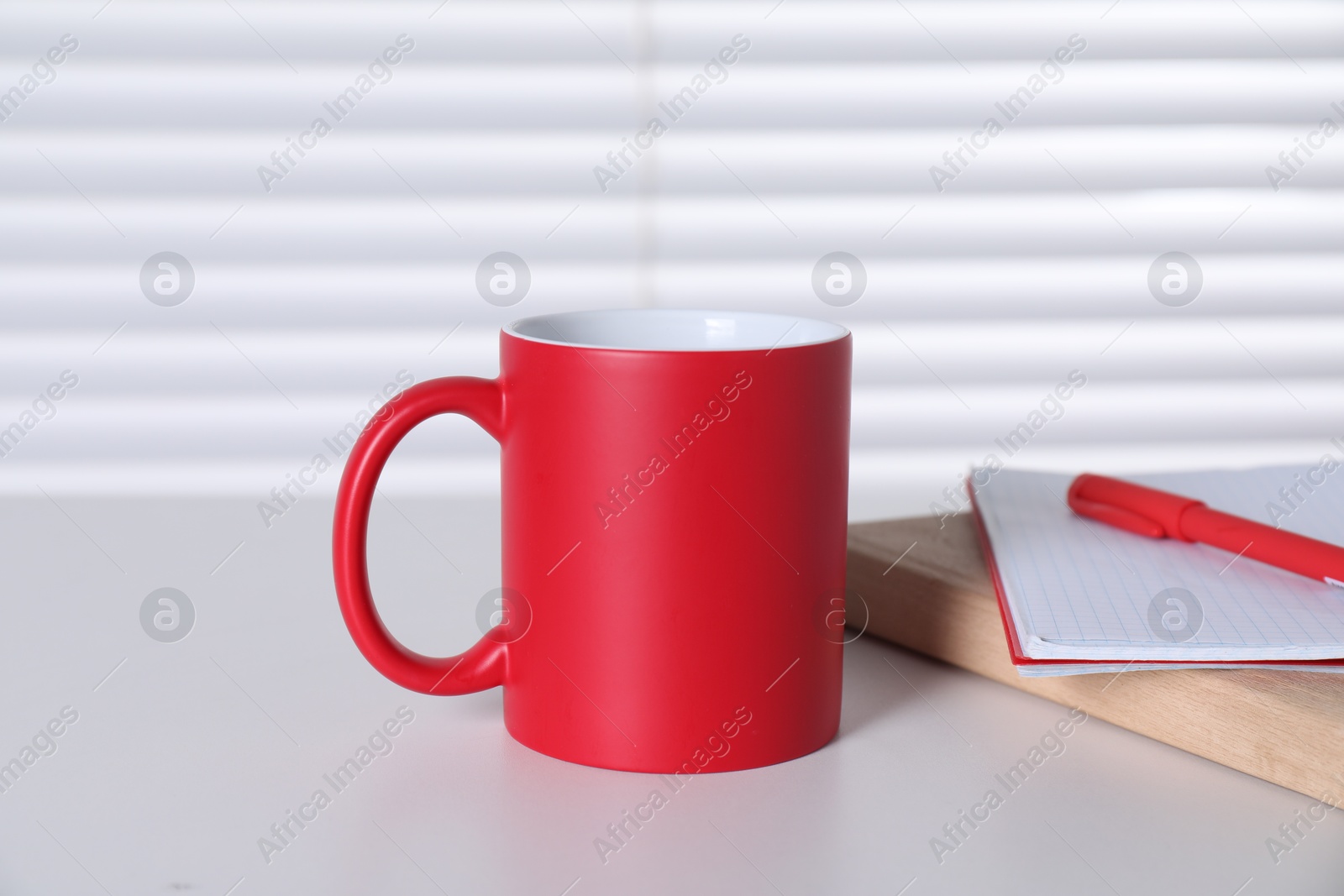 Photo of One blank red ceramic mug and notebooks on white table. Mockup for design