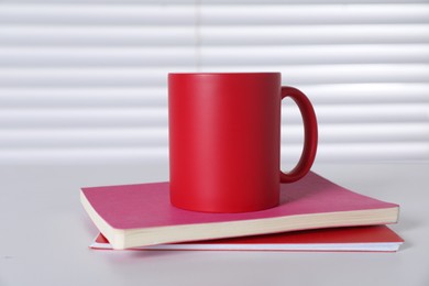 Photo of One blank red ceramic mug and notebooks on white table. Mockup for design