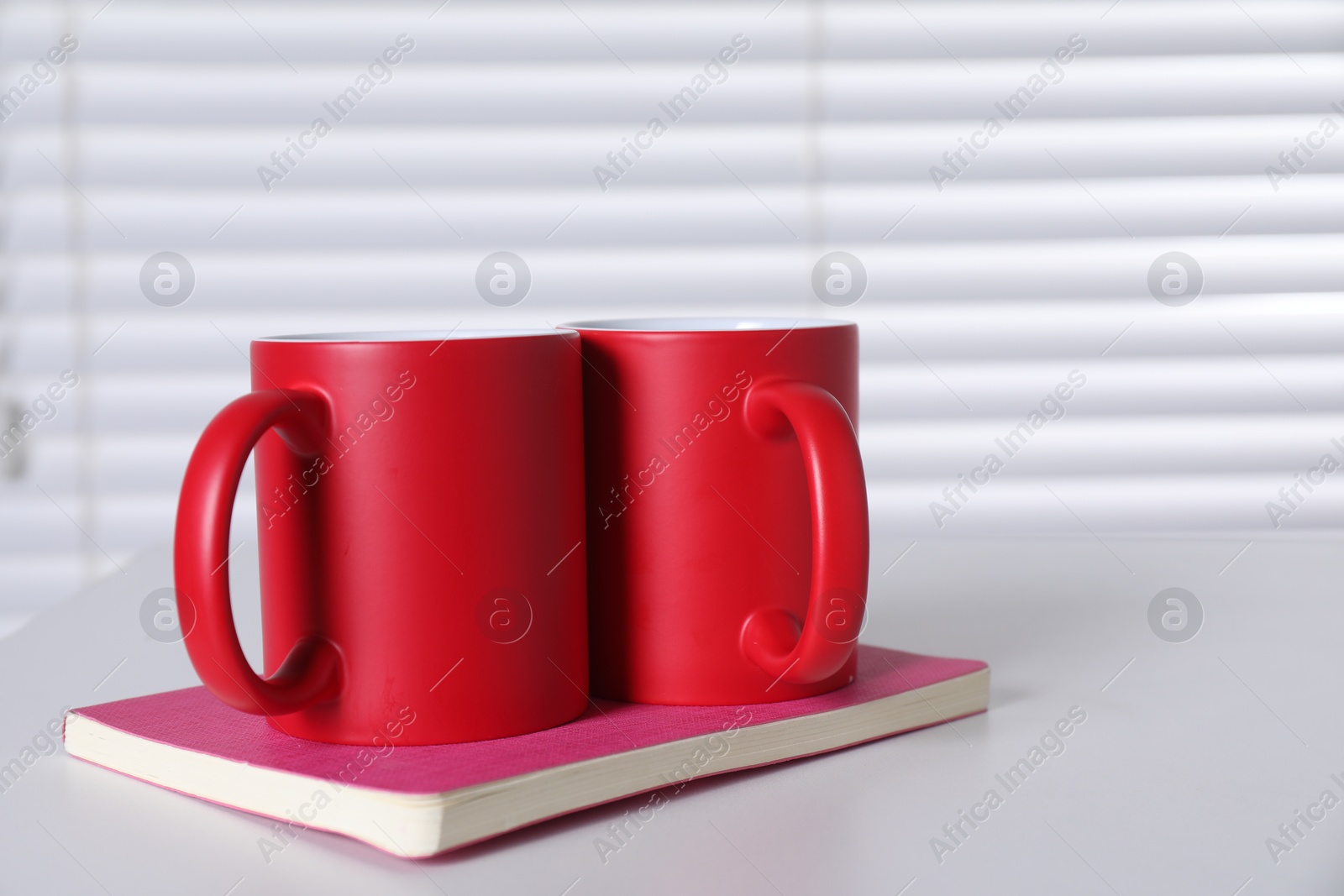 Photo of Blank red ceramic mugs and notebook on white table. Mockup for design