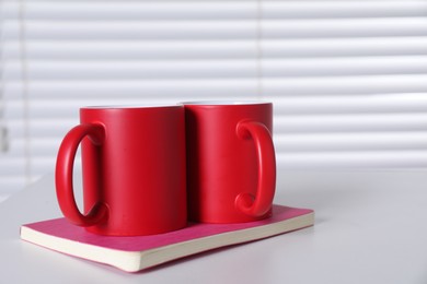 Photo of Blank red ceramic mugs and notebook on white table. Mockup for design