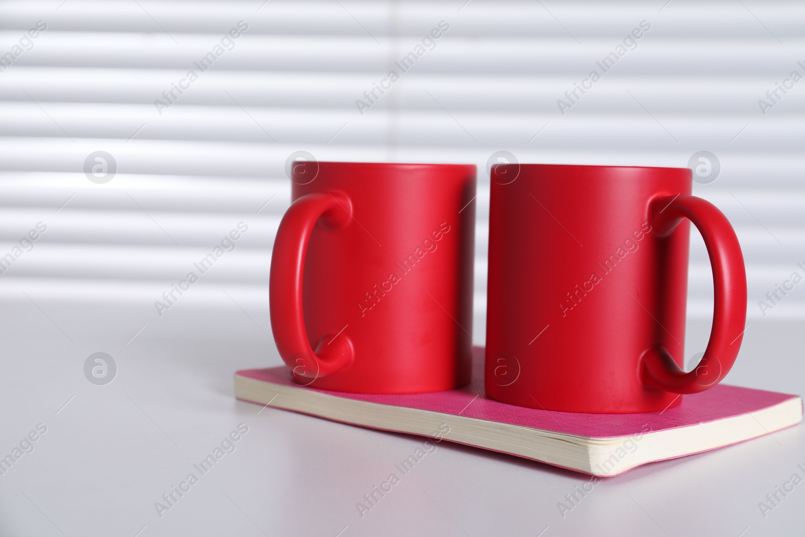 Photo of Blank red ceramic mugs and notebook on white table. Mockup for design