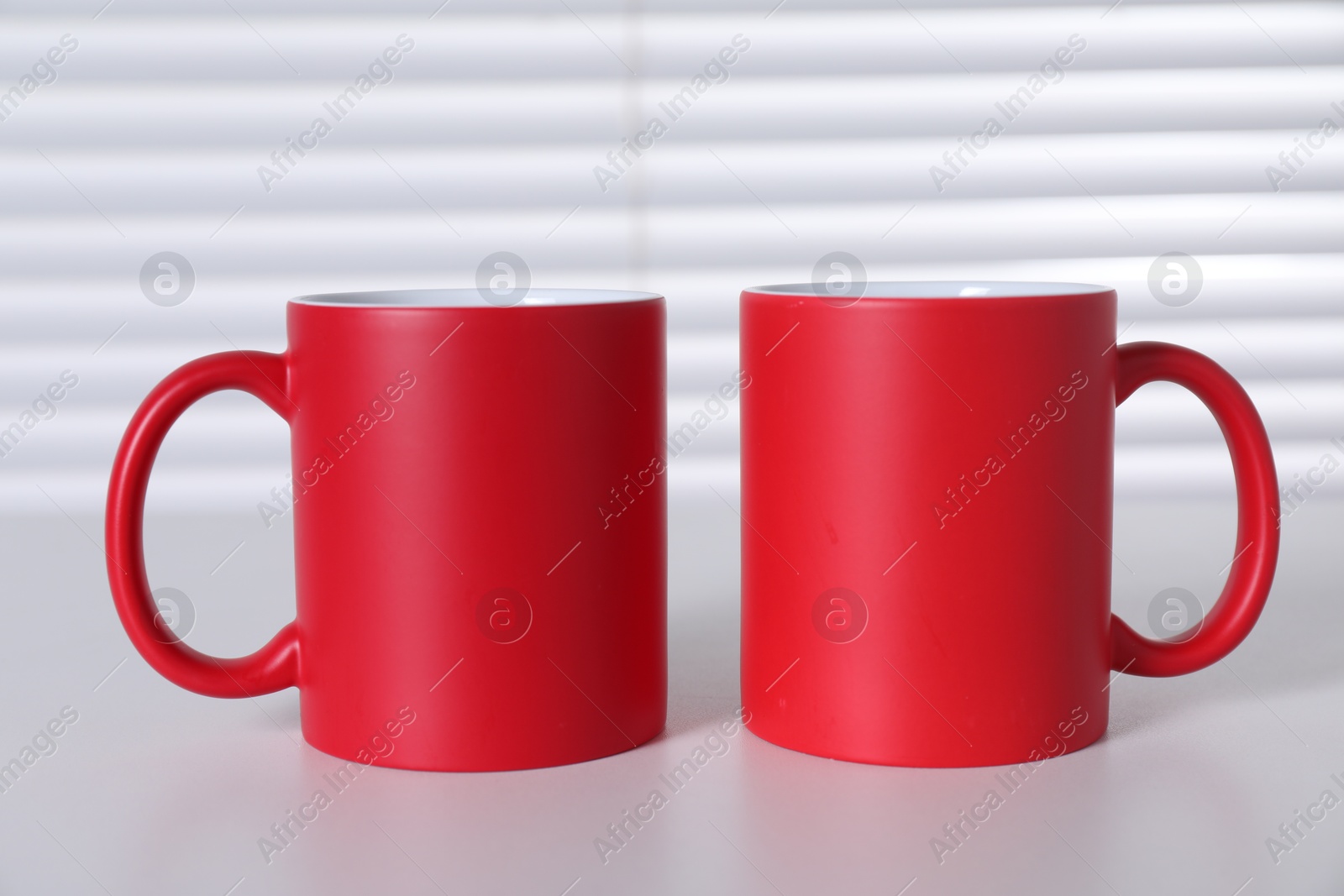 Photo of Blank red ceramic mugs on white table. Mockup for design