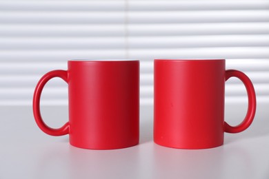 Blank red ceramic mugs on white table. Mockup for design