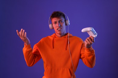 Unhappy young man with controller on violet background