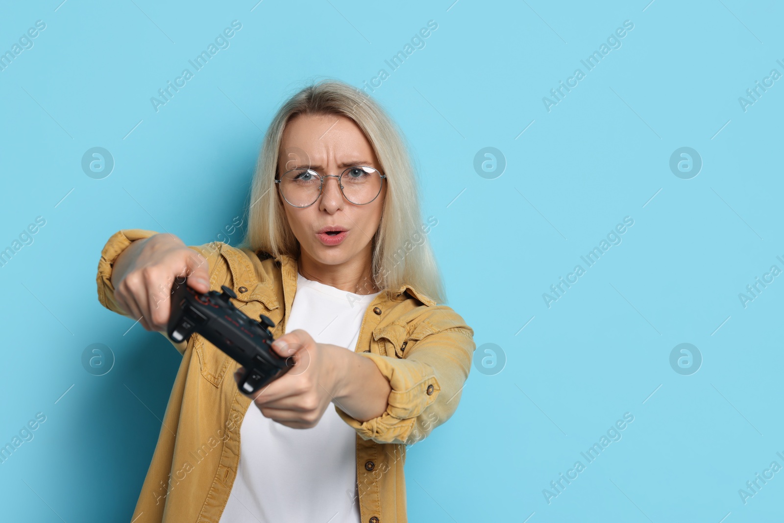 Photo of Woman playing video games with controller on light blue background, space for text